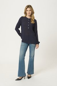 Blouse à manches longues marine avec une patte de boutonnage et des détails plissés, associée à un jean clair évasé et des escarpins noirs à bout pointu.