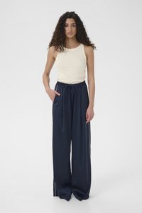 Marineblauwe satijnen broek met wijde pijpen en een trekkoord in de tailleband, voorzien van zijzakken, gecombineerd met een licht beige mouwloze top. Soepele textuur.