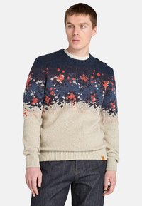 Sweter dziergany w kremowym kolorze z kolorowym geometrycznym wzorem w odcieniach granatu, czerwieni i bieli. Posiada okrągły dekolt oraz ściągacze przy mankietach i u dołu.