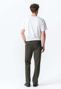 Hvid t-shirt med rund hals, parret med olivengrønne bukser med sidelommer og to baglommer. Sorte sko fuldender outfittet.