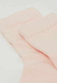 Lys rosa bomuldsstrømper med ribbet tekstur, der viser en glat overflade og foldede kantkanter, designet til komfort og slid.