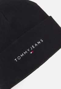 Gorro de punto negro con logo bordado "TOMMY JEANS" y un pequeño logo de acento tricolor en rojo, blanco y azul en el dobladillo.