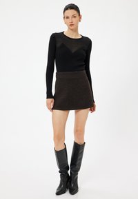 Zwarte geribbelde lange mouwen top met doorschijnende details, gecombineerd met een bruin textuur mini-jurk en kniehoge zwarte leren laarzen.