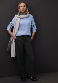 Vaaleansininen ribbineulottu neule, harmaa kuvioitu huivi ja tummanharmaat leveälahkeiset housut. Mustat kiillotetut saappaat viimeistelevät asun. Yksinkertainen tausta.