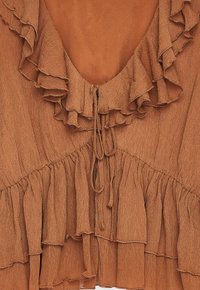 Roodbruin blouse met gelaagde rimpels rond een V-hals en striksluiting aan de voorkant, met een gestructureerde stof.