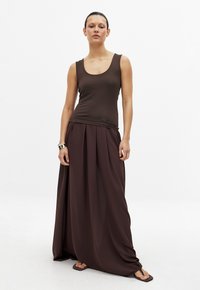 Brauner ärmelloser Oberteil kombiniert mit einem fließenden braunen Maxikleid. Glatte Textur, einfaches Design mit sanften Drapierungen und ohne sichtbare Muster.