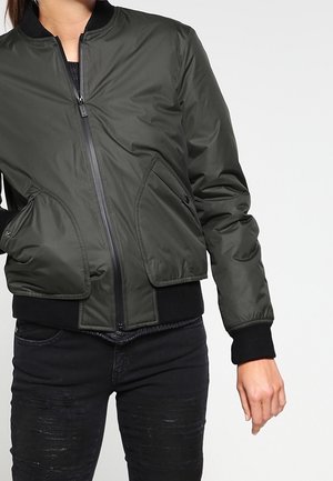 Person wearing a dark green bomber jacket with black ribbed cuffs and hem, paired with black distressed jeans.