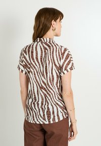 Camisa de manga corta en tejido ligero con un patrón de rayas de cebra en marrón y blanco, con cuello y mangas enrolladas.