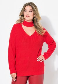 Pull rouge côtelé avec un col en V et un col choker. Manches longues, coupe ample, tissu tricoté texturé, et un ourlet qui couvre les hanches.