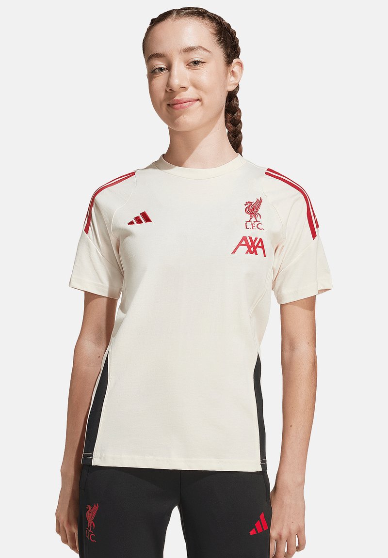 Maillot crème de Liverpool FC avec accents rouges, manches courtes, col rond, arborant le logo et le branding. Des panneaux latéraux noirs complètent le design.