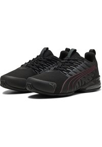 Czarne sportowe buty z siateczkową cholewką o teksturowanej powierzchni, odblaskowymi akcentami i grubą gumową podeszwą z lekkim obcasem. Wyraźne logo PUMA w kolorze czerwonym.