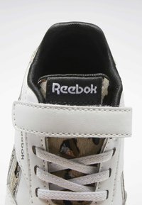 Baskets blanches avec panneau en tissu à motifs, languette en tissu, doublure noire et logo Reebok sur la languette. Comprend une bride velcro et des lacets.