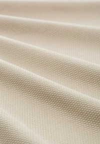 Tessuto di colore crema con una texture a motivo esagonale, che mostra sottili ondulazioni e una finitura liscia e morbida.
