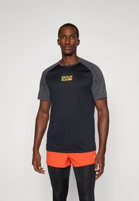 Svart kortermet atletisk skjorte med grå raglanermer, med "BERLIN RUN"-logo i gult. Glatt stoff, sportslig passform, kombinert med oransje shorts.