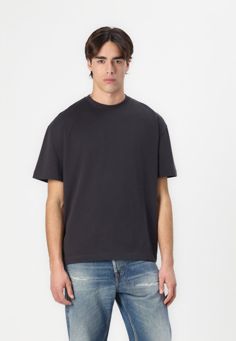 Dark gray cotton t-shirt with a crew neck, short sleeves, and a relaxed fit. Worn with distressed light blue jeans.