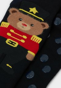 Námořnické ponožky s medvědem v červeném uniformě se žlutými akcenty. Texturované tečky s lesklým povrchem na podrážce pro grip.