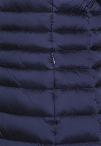 Chaleco acolchado navy con diseño de costuras horizontales, material ligero y un pequeño bolsillo con cremallera. Textura suave y lisa.