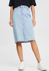 Vaaleansininen farkuhame, jossa on suoraviivainen leikkaus, edessä napit ja vyölenkit. Yhdistettyinä valkoisiin tennareihin rennon ilmeen saavuttamiseksi.