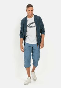 Navy knitted cardigan over a white t-shirt with a black graphic, paired with light blue cargo shorts and white sneakers.