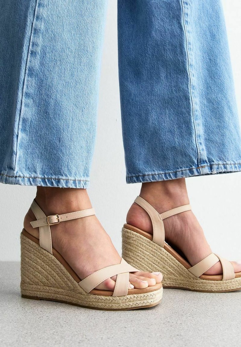 Sandales à talon compensé en toile beige avec des sangles croisées et une boucle à la cheville, dotées d'une semelle en jute tissée et d'une texture lisse semblable au cuir.