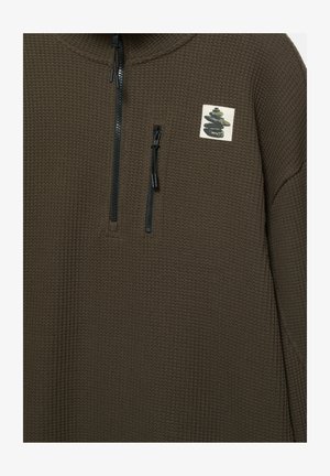 Bruine pullover met ritssluiting, gemaakt van een textuurrijke wafelkatoen, met een klein grafisch embleem en zwarte ritssluitingdetails.