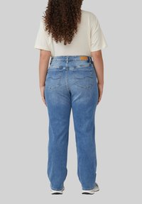 Jean bleu taille haute, coupe droite avec un délavage, deux poches arrière et une peau de cuir sur la ceinture. Texture en denim douce.