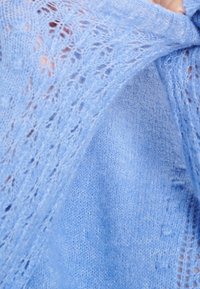 Ljusblått stickat plagg som visar en spetsstruktur med ett fint, luftigt mönster; tyget verkar mjukt och ömtåligt.