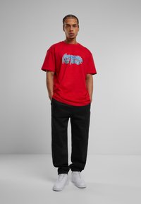 Piros pamut póló kék grafikai szöveggel, fekete melegítőnadrág és fehér sneakers. A póló laza szabású és rövid ujjú.