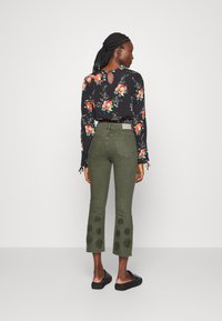 Blusa preta de flores com mangas longas e detalhe em forma de chave nas costas, combinada com calças cropped verde-oliva apresentando bordado floral na bainha.