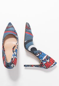 Chaussures à talons hauts imprimées avec un design bleu, rouge et noir, pointe aigüe et talon aiguille. Découpe sur le côté ouvert.