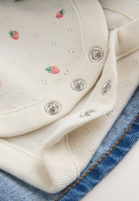 Cream-colored knitted fabric with small pink strawberry patterns and silver snap buttons, layered over blue denim with orange stitching.
