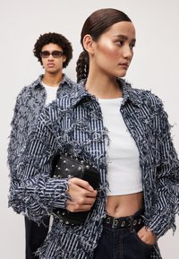 Iedragts džinsu jaka ar tumši ziliem un baltiem svītrām, ar metāla pogu uzsvariem, kombinēta ar melnu studētu maku un pieguļošu baltu topu.