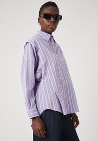 Light purple striped oversized shirt with a collared neckline and long sleeves. Made of a smooth fabric, featuring button cuffs.