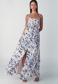 Robe maxi en tissu léger, présentant une base blanche avec des taches abstraites bleu marine, un col bateau, des bretelles spaghetti et une fente haute sur la cuisse.