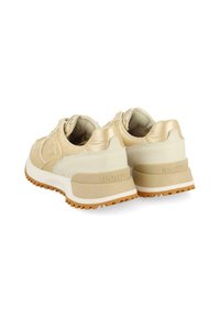 Zapatillas beige con un upper de lona texturizada, acentos brillantes y una suela de goma resistente con bandas de agarre. Marca en el talón.