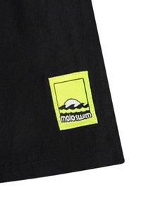 Melnā auduma izstrādājums ar taisnstūrveida, spilgti dzeltenu ielāpu, uz kura ir logotips, kas attēlo abstraktu vilni un tekstu "molo swim."