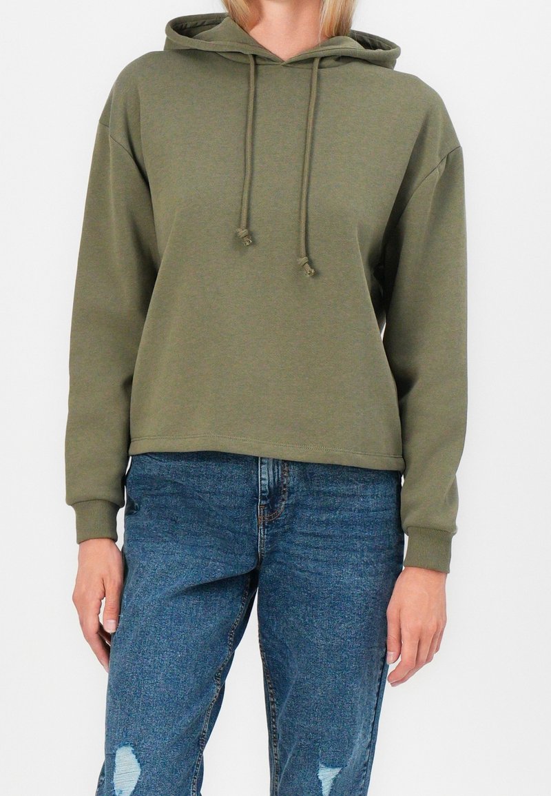 Sweat à capuche court vert olive avec capuche à cordon de serrage, manches longues, poignets côtelés et texture douce. Assorti à un jean bleu délavé déchiré.