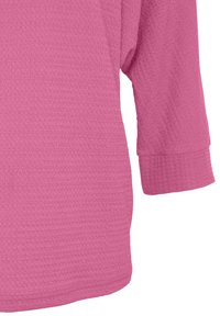 Rosa strukturierte Bluse mit 3/4-Ärmeln, die ein Gittermuster und einen weiten, runden Ausschnitt aufweist. Aus weichem Strickstoff.