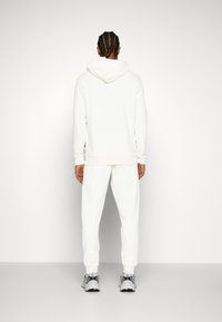 Hvid hættetrøje med snøre og ribbede manchetter, parret med matchende sweatpants. Glat, tekstureret stof, præsenteret med sporty sneakers.