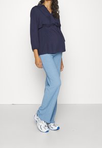 Marinblus med v-ringning och rynkad midja, i kombination med ljusblå strukturerade utsvängda byxor och silverfärgade sneakers med blå detaljer.