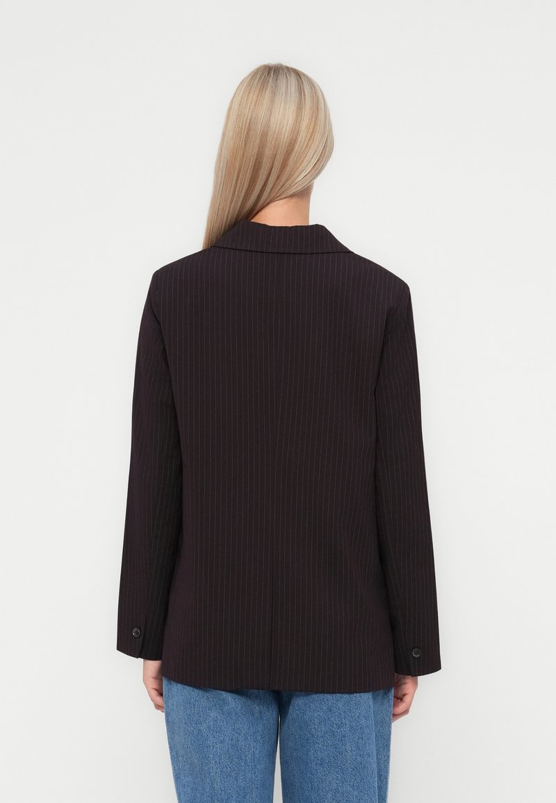 Blazer nero a righe con una vestibilità su misura, reverse a punta e polsino con un solo bottone. Texture liscia, abbinato a denim blu.