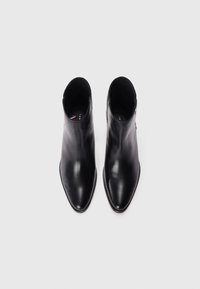 Botas de cuero negras hasta el tobillo con un diseño de puntera afilada. Cuentan con un panel elástico texturizado en el tobillo y acentos de hardware mínimos.