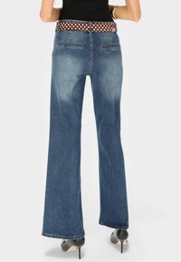 Niebieskie dzwony z denimu z wysokim stanem, wyposażone w brązowy pasek w groszki, dwie tylne kieszenie oraz czyste wykończenie na dole.