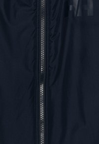 Giacca blu navy con una texture liscia e opaca, dotata di una zip centrale con denti metallici e un logo stampato in nero.