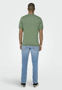 T-shirt verde a maniche corte con un design semplice, abbinato a jeans blu chiaro. La t-shirt ha un collo rotondo e una vestibilità attillata.