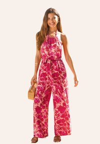 Jumpsuit s halterovým výstřihem v růžovém a fuchsiovém květinovém vzoru, se širokými nohavicemi a staženým pasem, doplněný dřevěnou kabelkou.