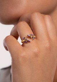 Anello d'oro con pietre a forma di marquise viola e piccoli accenti chiari, progettato per assomigliare a foglie, indossato su una mano.