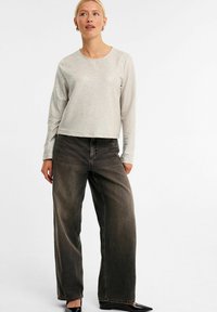 Lys grå, tekstureret langærmet top med rund halsudskæring, parret med brede, mørkegrå jeans og sorte spidse flade sko.