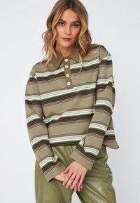 Polo-shirt à rayures marron et vert à manches longues avec un col, comportant cinq boutons décoratifs et un tissu texturé. Associé à un pantalon vert brillant.