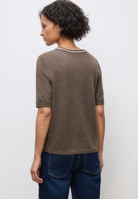 Maglione marrone a maniche corte con finitura testurizzata e un semplice collo rotondo, caratterizzato da un sottile bordo bianco lungo il collare.